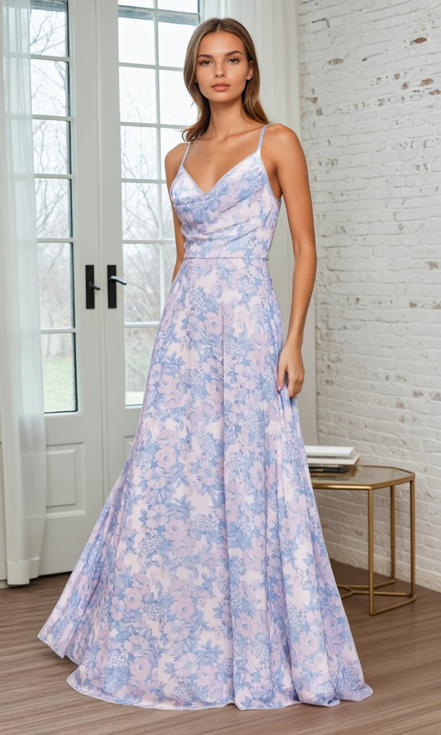 A woman poses indoors in the Floral-Print Long A-Line Prom Dress: Ladivine 7444, a sleeveless gown with a cowl neckline in pastel purple and blue hues, standing before glass doors and a white brick wall.